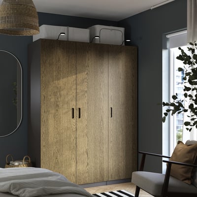 Modernes Schlafzimmer mit hohem Kleiderschrank, Spiegel, Lampe und Sessel.