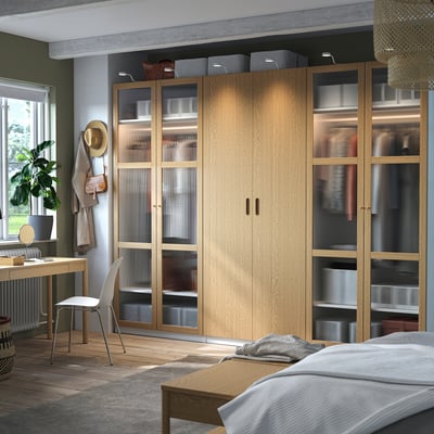 PAX-Kleiderschrank mit hellem Holz, Glastüren, Regalen und Schreibtisch mit Stuhl.