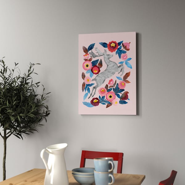 Kunstdruck mit Hirschen und Blumen, gerahmt an der Wand, neben Holztisch mit Pflanze, Tassen und Schale.
