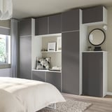 Modernes Schlafzimmer mit grauem PLATSA-Stauraum, weißem Bett, Spiegel, geometrischem Kissen.