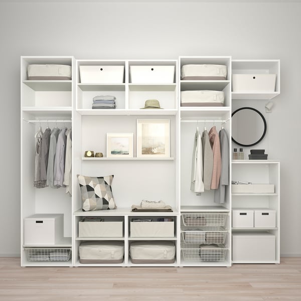 Moderner weißer Kleiderschrank mit Regalen, Schubladen und Hängefläche für Kleidung. Enthält Dekorationsartikel wie Kissen, Hut und Kunstrahmen.