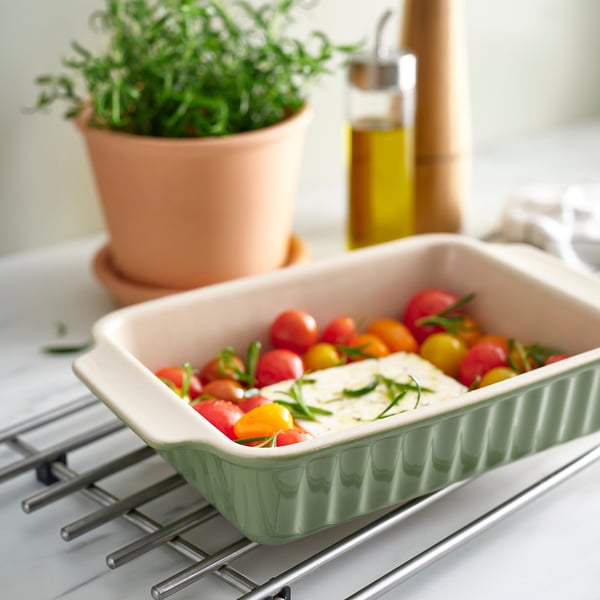 Schüssel aus grünem Steinzeug mit Kirschtomaten und Kräutern auf dem Herd.