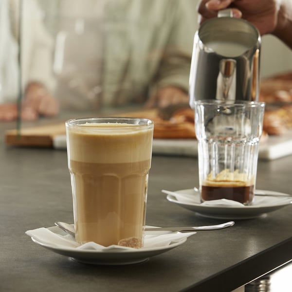 Zwei Gläser Kaffee auf Untertassen mit Löffeln und Servietten, eines davon aus einem Cafetiere.