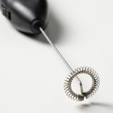 Schwarzer Milchaufschäumer mit Metallspirale auf weißem Hintergrund, kompakt für eine einfache Kaffeezubereitung.