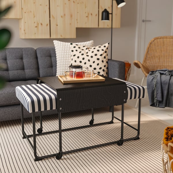 Modernes Wohnzimmer mit schwarz gestreifter RÄVSAL-Bank, grauem gepolstertem Sofa, Holzschränken und Korbstuhl auf gestreiftem Teppich.