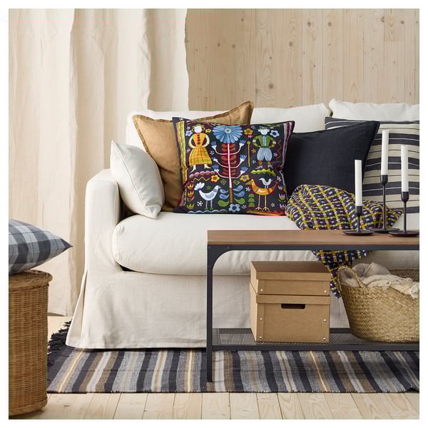 Wohnzimmer mit weißem Sofa, bunten Kissen, gestreiftem Teppich und Holzwänden.