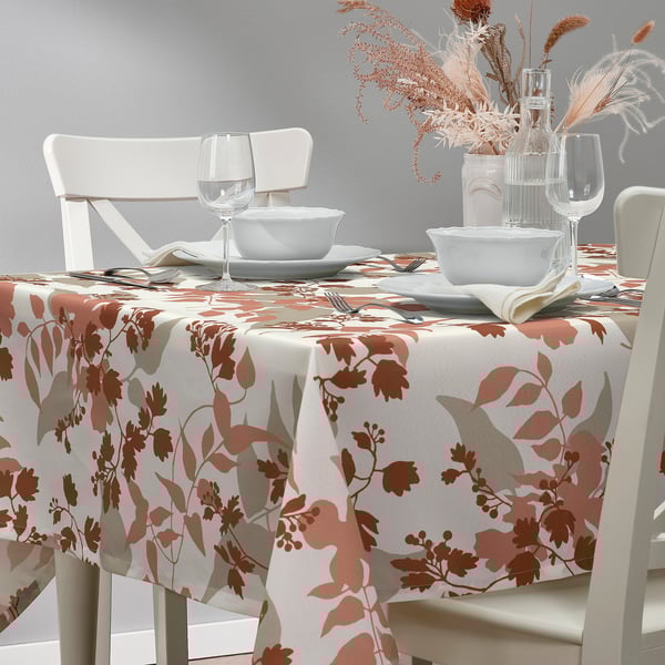 Herbstliches Esszimmer mit Tischdecke und Stühlen mit Blattmuster, weißem Geschirr und getrockneten Blumen.
