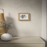 Ein minimalistischer Raum mit abstrakter Kunst an einer grauen Wand, beiger Schublade, Korb und Blumen.