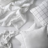 Weißes Bettwäsche-Set aus recyceltem Polyester, einschließlich Decke und Kissenbezügen, auf weißem Laken mit Gittermuster.