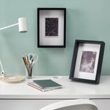 Schreibtisch mit Kunstrahmen, Lampe und Schreibwaren. Die Rahmen können stehen oder hängen, mit säurefreien Halterungen.