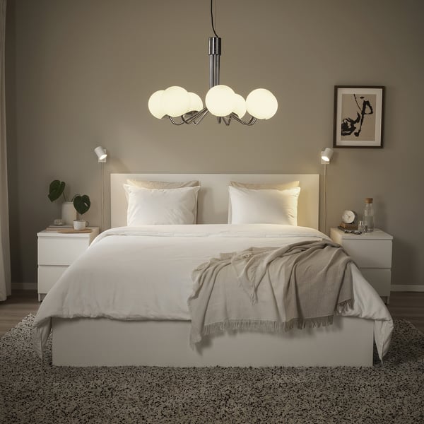 Modernes Schlafzimmer mit Kronleuchter aus Chrom und Glas, weißer Bettwäsche, grauem Überwurf, Nachttischen, Wandleuchten.