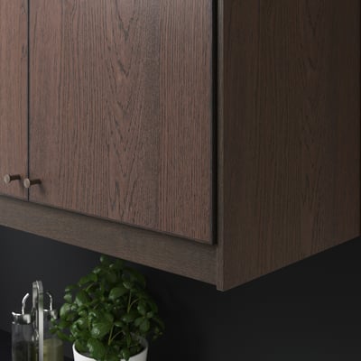 Schrank aus dunklem Holz mit Metallgriffen; Pflanze unten.