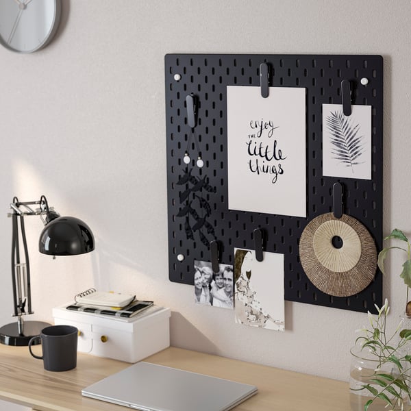 Schreibtisch mit SKÅDIS-Stecktafel mit Fotos und Notizen; Laptop, Lampe, Tasse und Pflanze auf dem Schreibtisch.