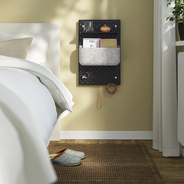 Schlafzimmer mit SKÅDIS Steckbrett-Organizer am Bett, mit Accessoires und Notizen in der Nähe eines Fensters.