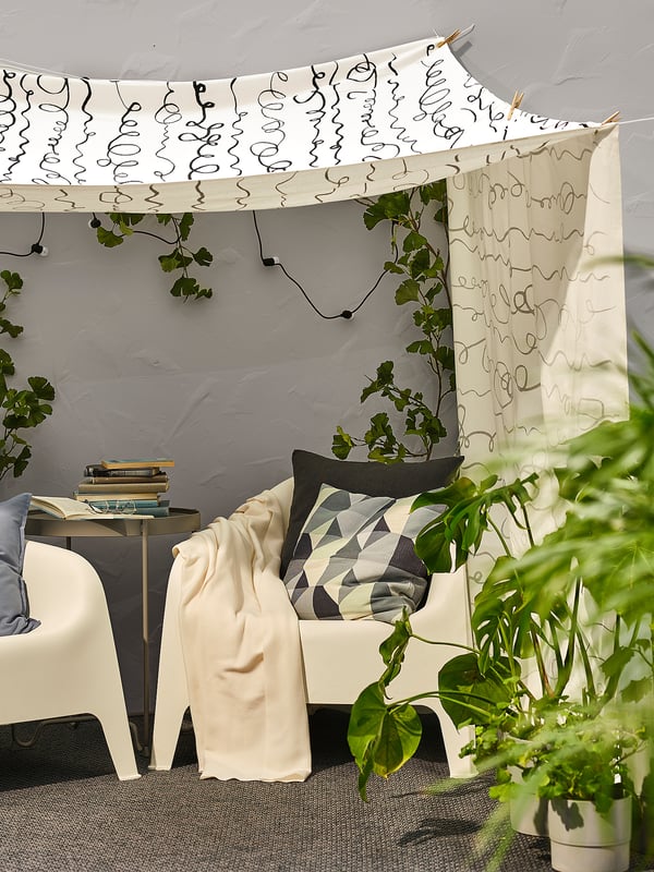 Gemütliches Indoor-Setup mit weißen SKARPÖ-Sesseln, gemusterten Kissen, Pflanzen und Himmelzelt mit Lichterketten.
