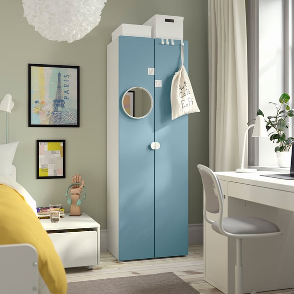 Modernes Schlafzimmer mit blauem SMÅSTAD-Kleiderschrank, Spiegel, gelbem Stuhl und Schreibtisch. Zur Dekoration gehören Bilder und eine Pflanze für ein gemütliches Ambiente.