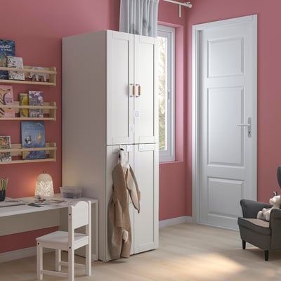 Ein Kinderzimmer mit einem weißen SMÅSTAD-Kleiderschrank, Regalen und Schreibtisch. Rosafarbene Wände, Holzboden.