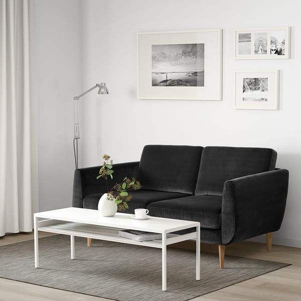 Modernes Wohnzimmer mit dunkelgrauem Samtsofa, weißem Couchtisch und schwarz-weißer Wandkunst.