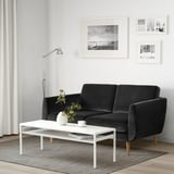 Modernes Wohnzimmer mit dunkelgrauem Samtsofa, weißem Couchtisch und schwarz-weißer Wandkunst.