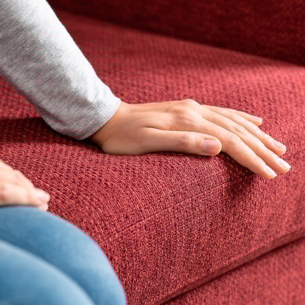 Nahaufnahme von Händen, die auf einem weichen roten Sofa ruhen und Komfort und Qualität zeigen.