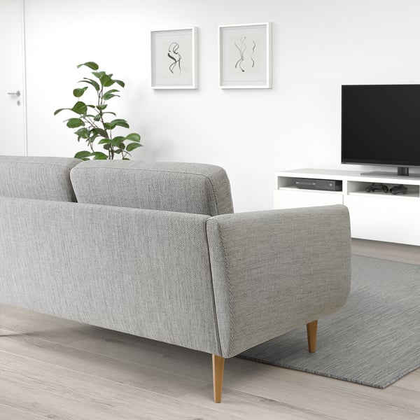 Modernes Wohnzimmer mit grauem SMEDSTORP-Sofa, Holzbeinen, Armlehnen und Kissen, Fernseher auf weißem Ständer, grüner Pflanze, abstrakter Wandkunst.