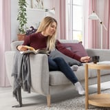 Eine Frau liest auf einem grauen SMEDSTORP-Sofa am Fenster ein Buch. Das Zimmer ist mit rosa Vorhängen und einer Pflanze geschmückt.