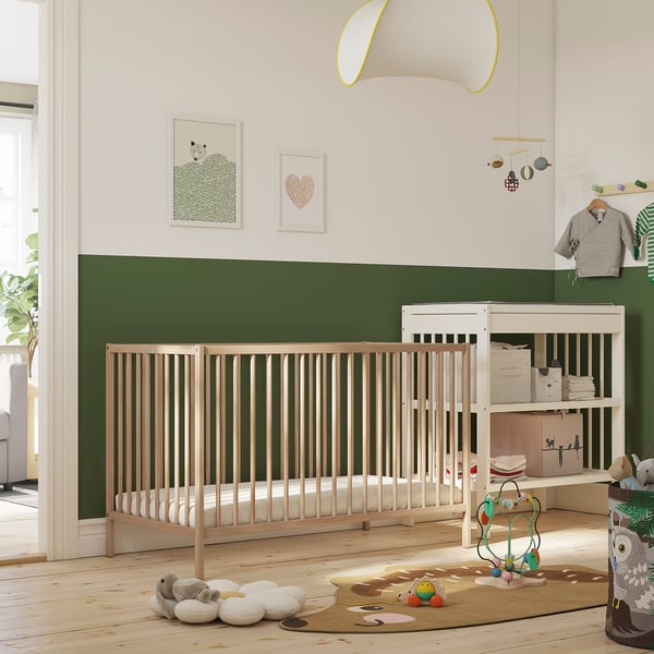 Helles Kinderzimmer mit SNIGLAR-Kinderbett , Wickeltisch, Spielzeug und Kunst. Kinderbett zentriert, größer als Spielzeug, kleiner als Rahmen.