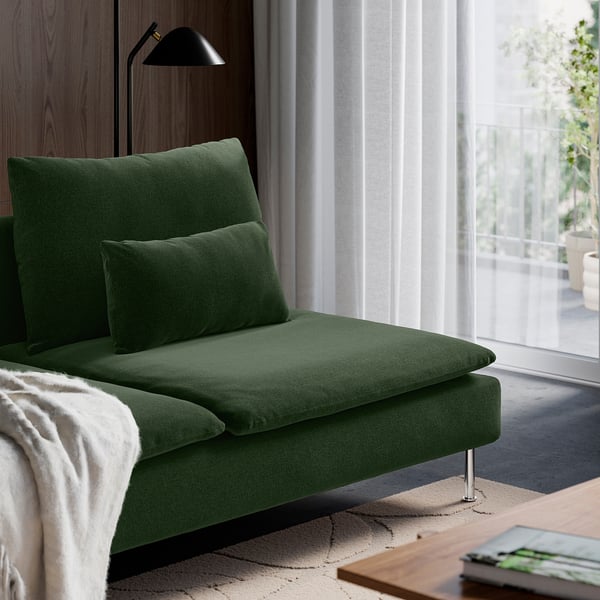 Eine grüne Stoffchaiselongue mit weichen Kissen, neben einem großen Fenster, bietet Entspannung und Komfort.