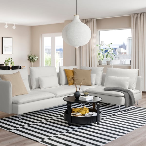 Minimalistisches Wohnzimmer mit weißer SÖDERHAMN-Sektion, schwarzem Couchtisch, gestreiftem Teppich und großem Fenster mit Blick auf die Stadt. Gemütliches und modernes Design.