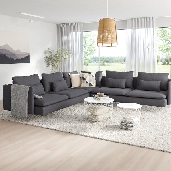 Modernes Wohnzimmer mit SÖDERHAMN-Sektion, geometrischen Kissen, weißen Couchtischen und großem Fenster mit grauen Vorhängen.