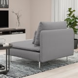 Eine Chaiselongue aus grauem Stoff mit einem grauen Kissen auf einem gemusterten Teppich in einem modernen Wohnzimmer.