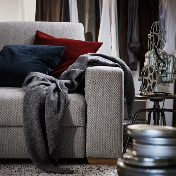 Modernes hellgraues SÖRVALLEN-Sofa mit dunklen Kissen und gemütlichem Überwurf, neben einem Vintage-Filmprojektor auf einem Ständer.