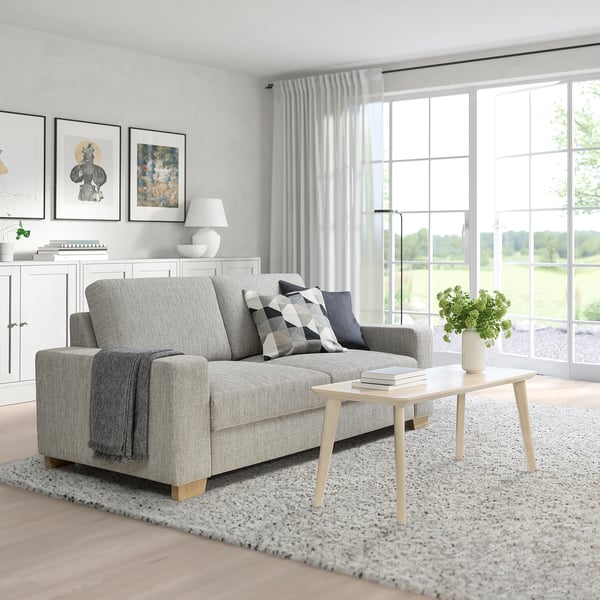 Modernes Wohnzimmer mit SÖRVALLEN-Sofa, Couchtisch, Büchern und Grün unter großen Fenstern.