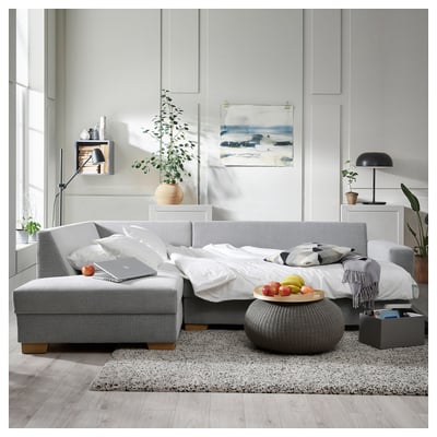 Modernes Wohnzimmer mit einem grauen SÖRVALLEN-Sofa mit weißen Kissen, grauer Ottomane und minimalistischem Dekor.