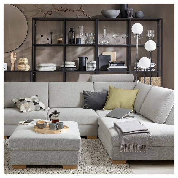 Modernes, minimalistisches Wohnzimmer mit grauem SÖRVALLEN Sektionssofa, Kissen, Couchtisch, stilvollen Regalen und Stehlampe.