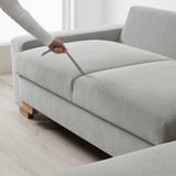 Person zieht Schlafsofaaufsatz heraus. Das hellgraue Sofa lässt sich in ein Bett verwandeln und zeigt eine funktionale Seitenverlängerung.