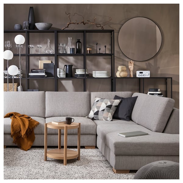 Modernes Wohnzimmer mit einem grauen SÖRVALLEN-Sofa, einem Beistelltisch aus Holz, schwarzen Kissen und einem Bücherregal mit Dekorationsgegenständen.