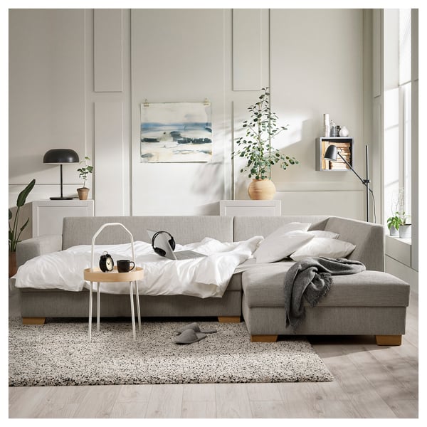Modernes, graues SÖRVALLEN-Sofa, minimalistisches Design mit weißen Kissen, schwarzer Lampe, Holztisch und gemütlicher Bettwäsche.