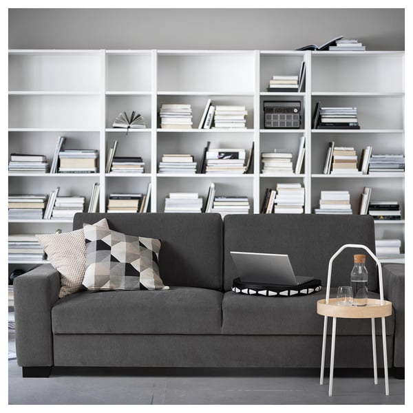 Modernes Wohnzimmer mit grauem SÖRVALLEN-Sofa, Kissen, Laptop und hölzernem Beistelltisch vor dem Bücherregal.