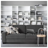 Modernes Wohnzimmer mit grauem SÖRVALLEN-Sofa, Kissen, Laptop und hölzernem Beistelltisch vor dem Bücherregal.