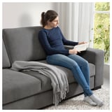 Entspannte Frau, die auf dunkelgrauem SÖRVALLEN-Sofa liest, Denim-Jeans, marineblaues Hemd, graue Decke, modernes, gemütliches Wohnzimmer.