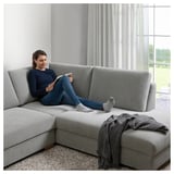 Frau liest auf modernem grauem SÖRVALLEN Sofa am Fenster. Das Sofa hat abnehmbare Kissen, die Frau trägt blau.