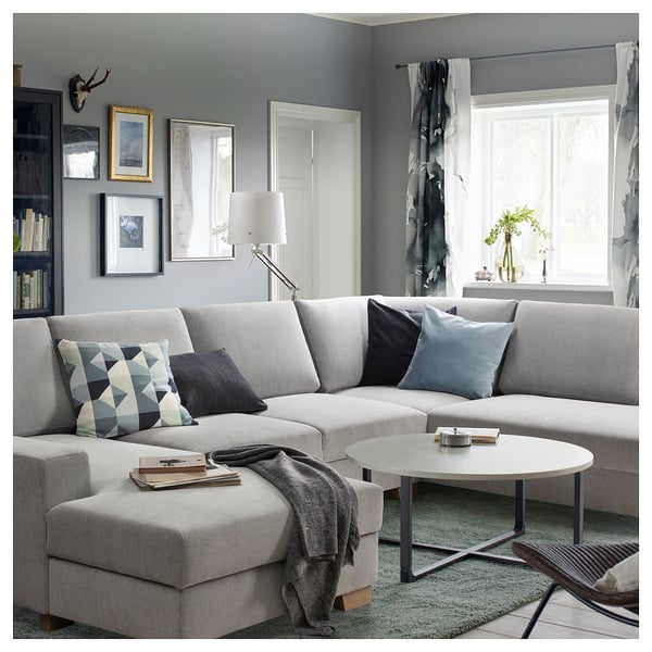 Modernes Wohnzimmer mit grauem SÖRVALLEN-Sofa, Kissen, Couchtisch, Lampe, Bücherregal und großen Fenstern.