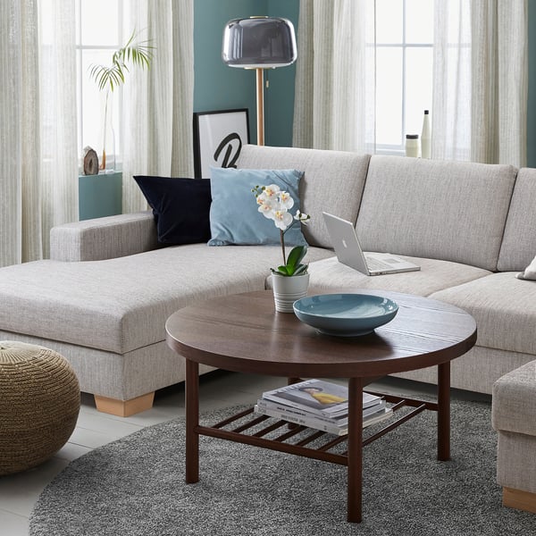 Modernes Wohnzimmer mit einem grauen SÖRVALLEN-Sofa, einem Couchtisch aus Holz, einem Laptop, einer Schale, einer Pflanze und einer Stehlampe.