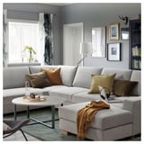 Modernes graues L-förmiges Sofa mit bunten Kissen, Couchtisch und gemütlicher Einrichtung in stilvollem Wohnzimmer mit großen Fenstern.