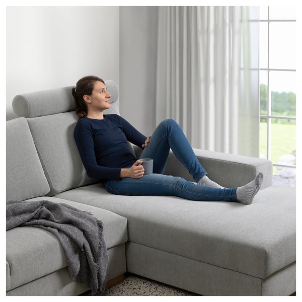 Eine Frau entspannt sich auf einem grauen SÖRVALLEN-Sofa und hält eine Tasse in der Hand, in der Nähe eines Fensters.