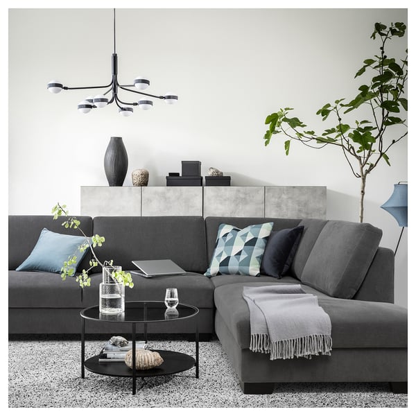 Modernes Wohnzimmer mit einem grauen SÖRVALLEN-Sofa, geometrischen Kissen, einem Couchtisch aus Glas und einer Hängeleuchte.