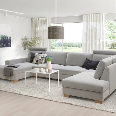 Modernes graues Sofa mit Chaiselongue, großen Fenstern, Couchtisch, Pflanzen, Lampe, Teppich.