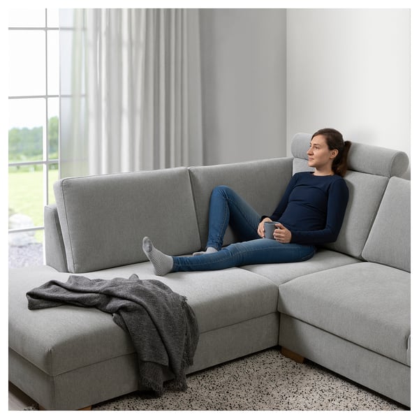 Eine Frau entspannt sich auf einem grauen SÖRVALLEN-Sofa in der Nähe eines Fensters.