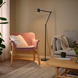 Gemütliches Wohnzimmer mit pfirsichfarbenem Stuhl, grauer Couch, Holztisch, schwarzer Stehlampe und grüner Pflanze.